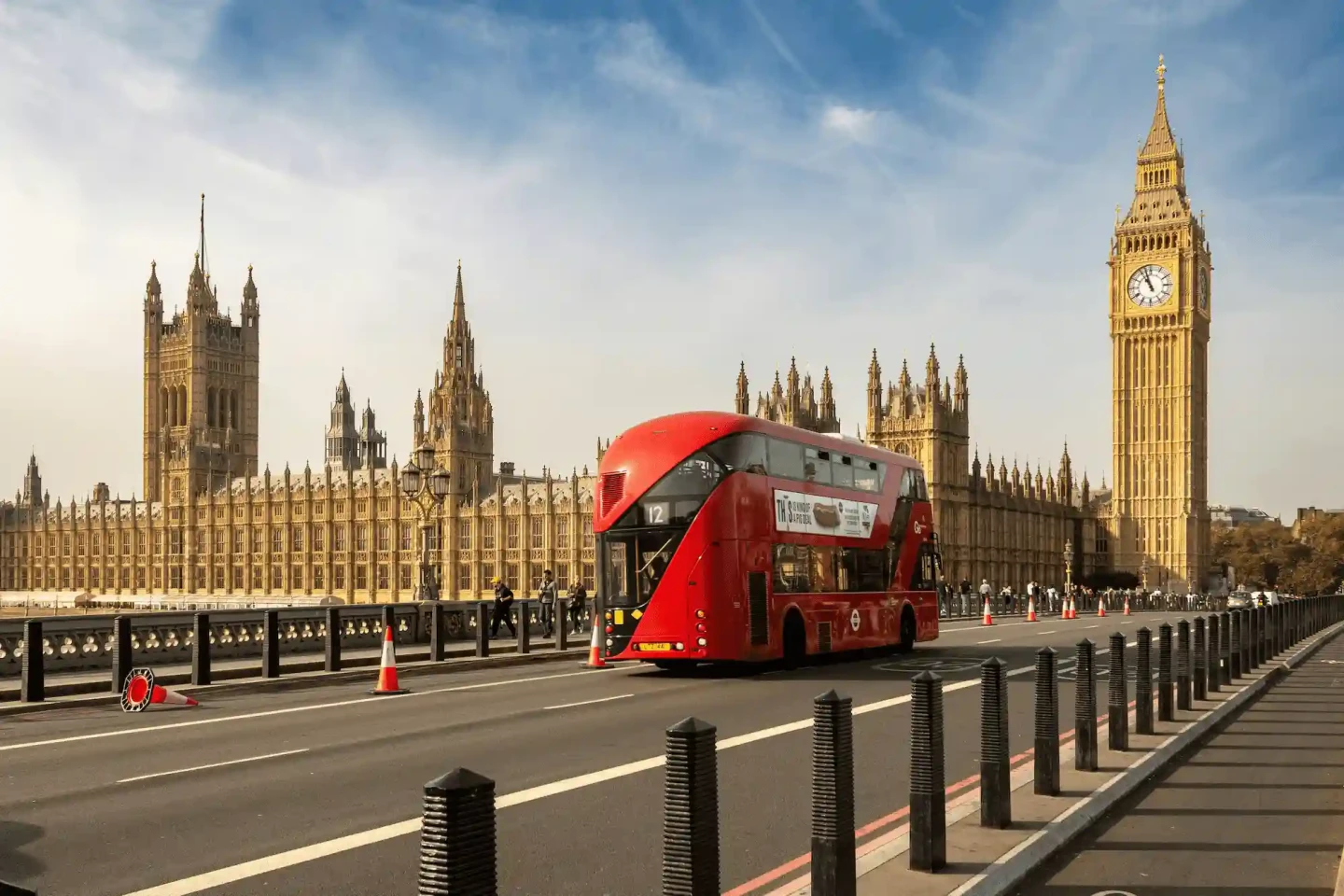 Red London bus driving near Big Ben and the Houses of Parliament in central London. Stayprime Serviced Apartments