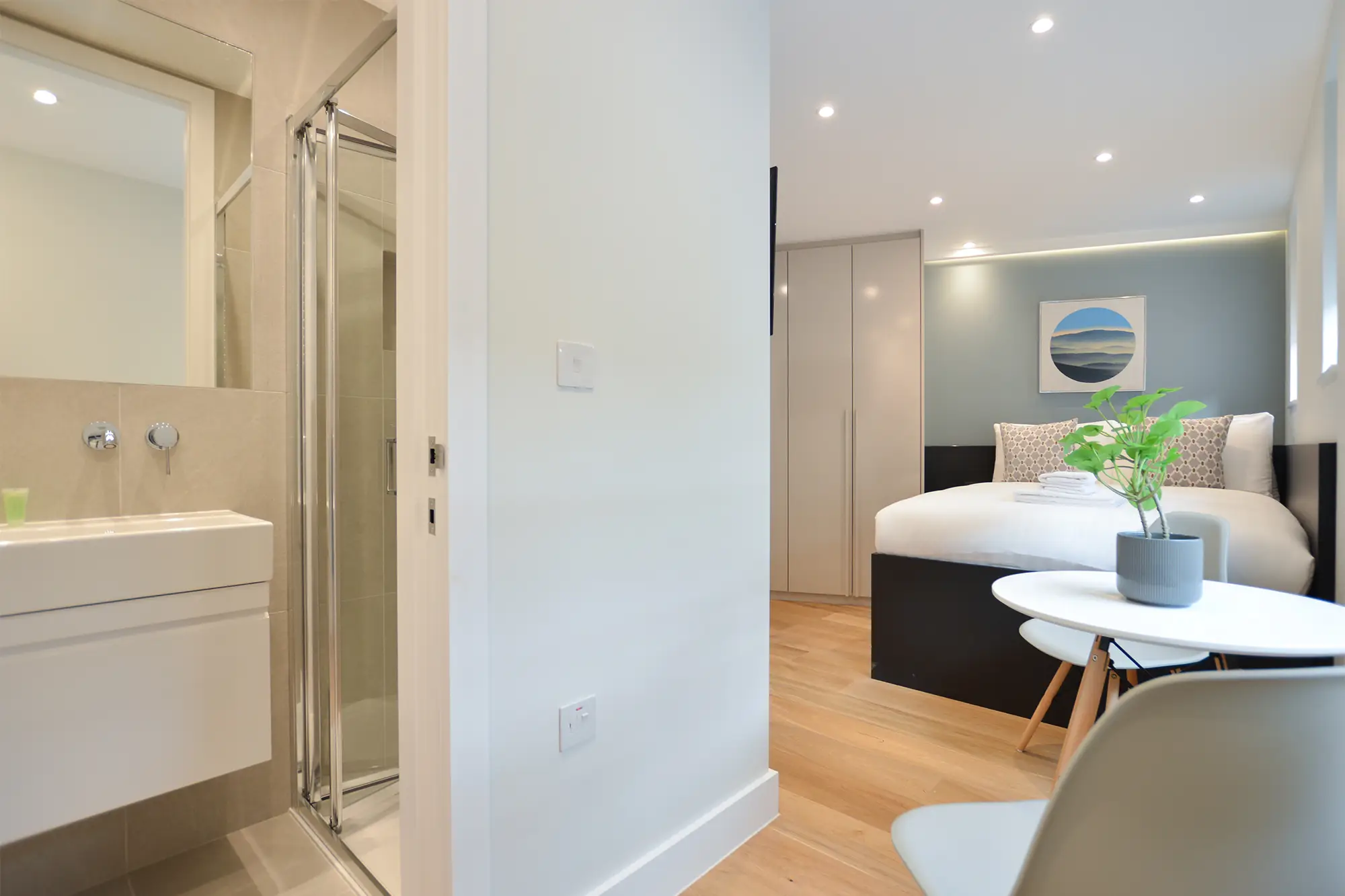 A modern small studio apartment in Marylebone with a plush double bed, a cozy dining area, hardwood floors with underfloor heating, and a separate elegant private bathroom with a shower