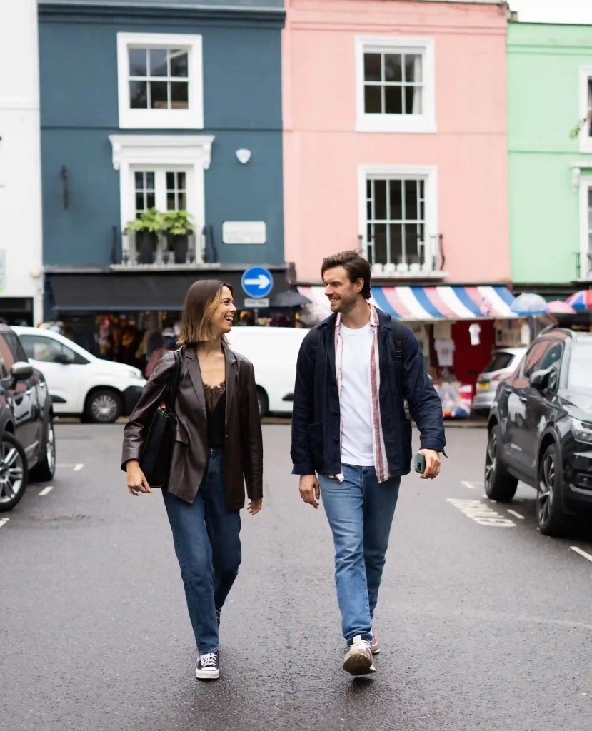 A stylish one-bedroom serviced apartment overlooking Portobello Road, Notting Hill, with a staircase leading to the upper level, a modern sleeping area with a plush double bed, wooden floors, underfloor heating, and an entrance to an elegant private bathroom with a shower