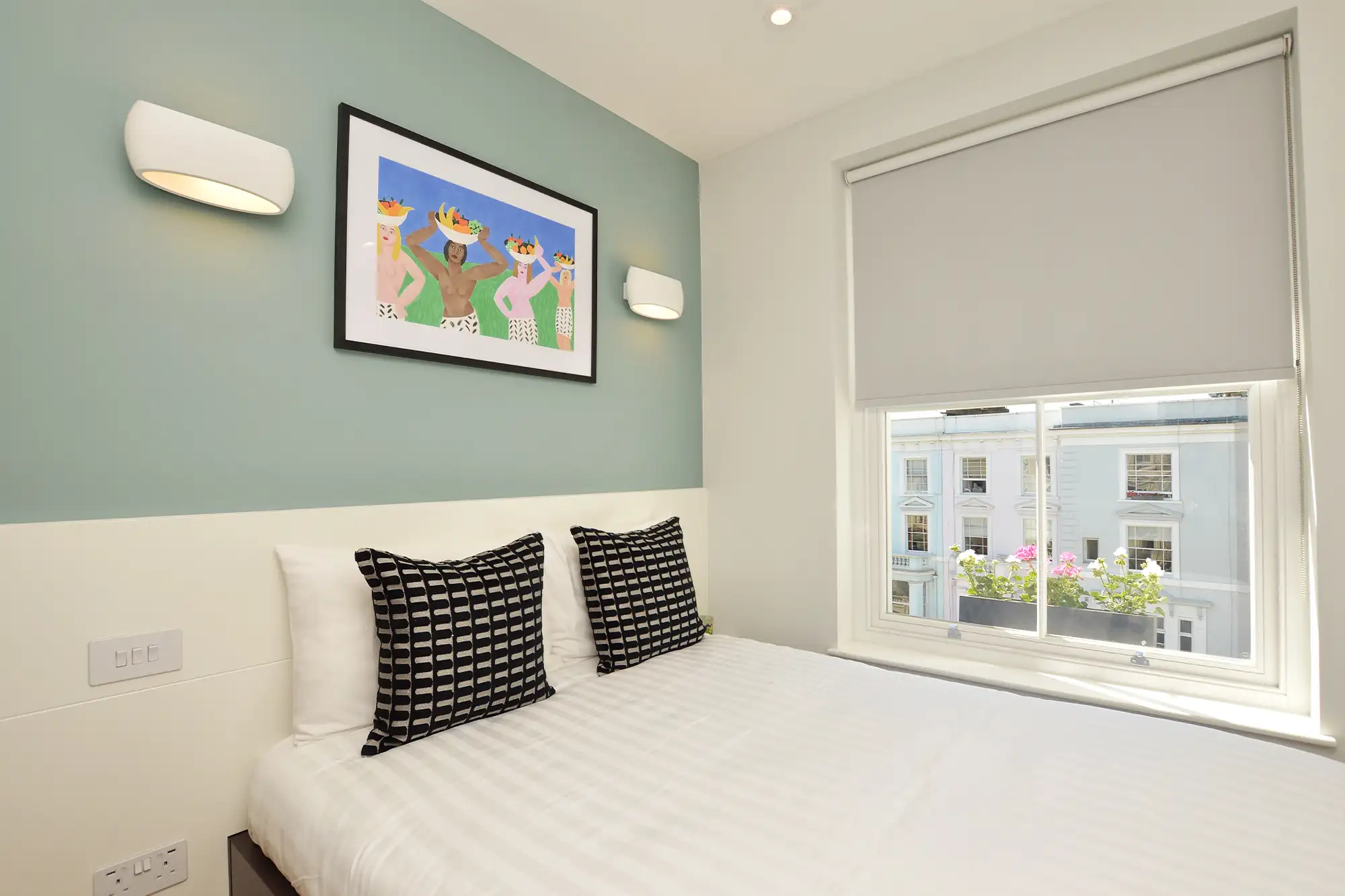 A modern one bedroom serviced apartment with a stylish sleeping area, a plush double bed, wooden floors, and underfloor heating, with a window overlooking Portobello Road in Notting Hill