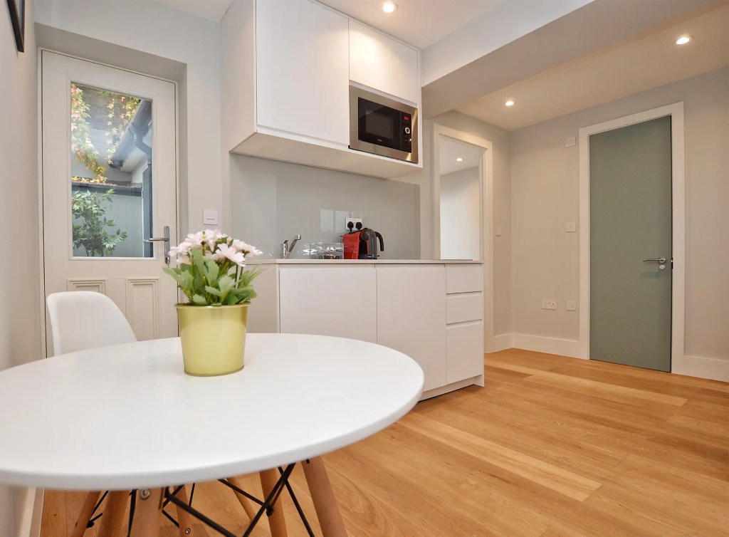An airy and spacious studio apartment in Notting Hill, with wooden floors, a modern kitchenette, a dining area, and access to a cozy private yard.