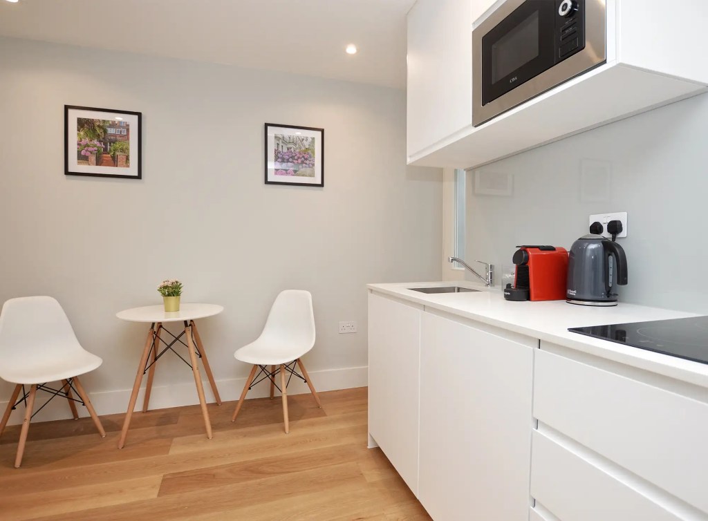 An airy and spacious studio apartment in Notting Hill, with wooden floors, a modern kitchenette, a dining area, and access to a cozy private yard.
