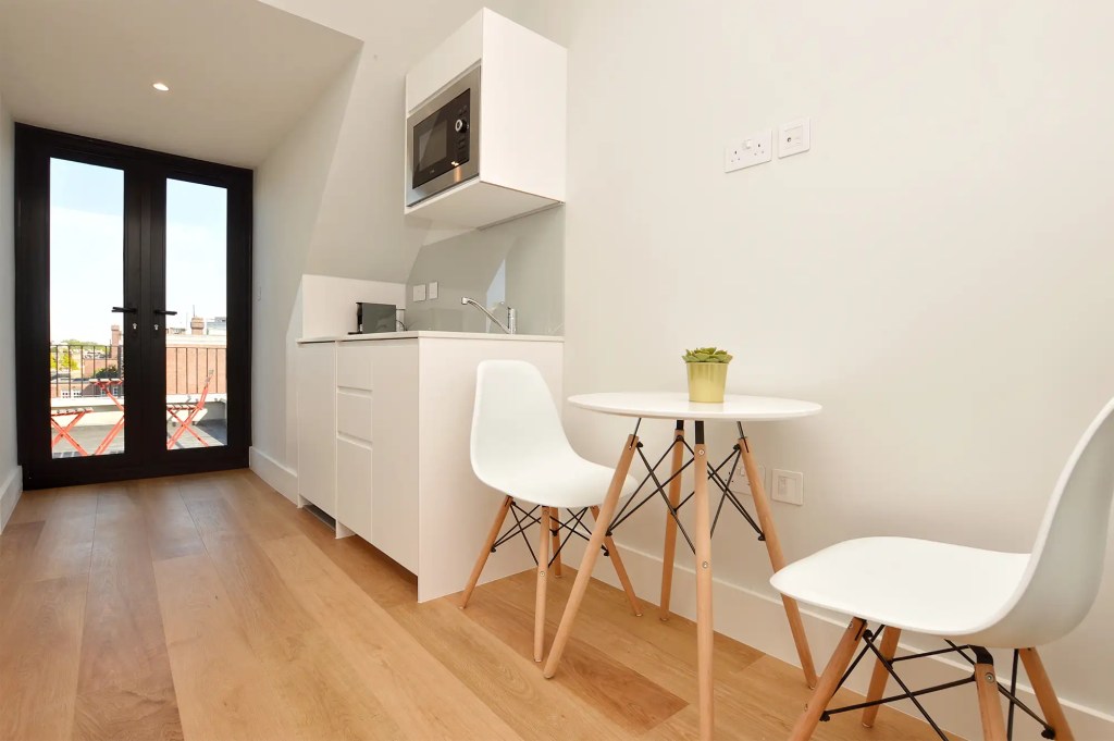 A stylish one-bedroom serviced apartment overlooking Portobello Road, Notting Hill, with a staircase leading to the upper level, a modern sleeping area with a plush double bed, wooden floors, underfloor heating, and an entrance to an elegant private bathroom with a shower