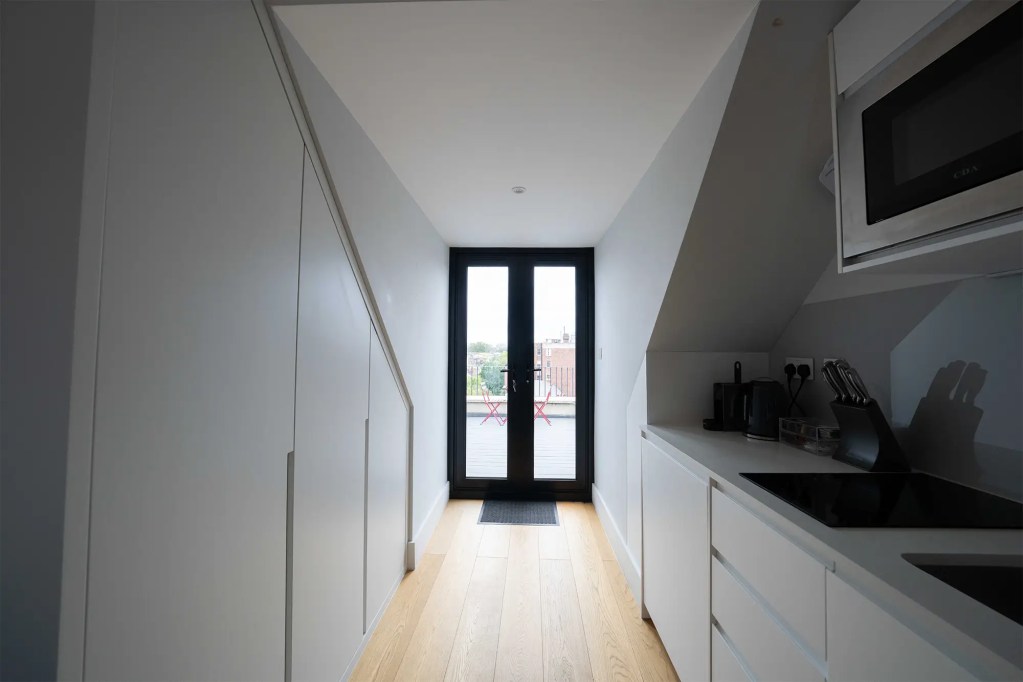 A stylish one-bedroom serviced apartment overlooking Portobello Road, Notting Hill, with a staircase leading to the upper level, a modern sleeping area with a plush double bed, wooden floors, underfloor heating, and an entrance to an elegant private bathroom with a shower