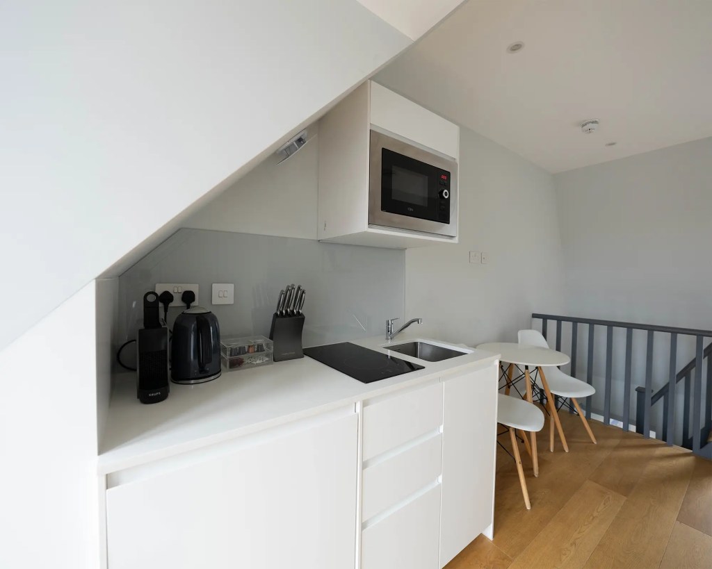 A stylish one-bedroom serviced apartment overlooking Portobello Road, Notting Hill, with a staircase leading to the upper level, a modern sleeping area with a plush double bed, wooden floors, underfloor heating, and an entrance to an elegant private bathroom with a shower