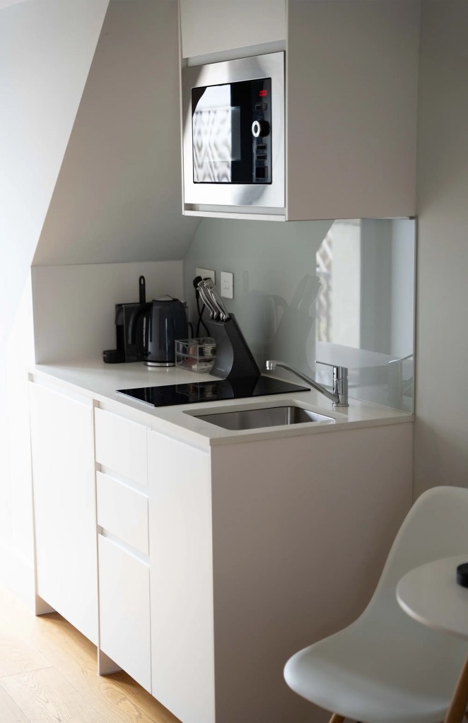 A stylish one-bedroom serviced apartment overlooking Portobello Road, Notting Hill, with a staircase leading to the upper level, a modern sleeping area with a plush double bed, wooden floors, underfloor heating, and an entrance to an elegant private bathroom with a shower