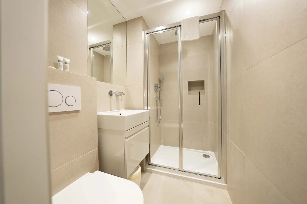 A stylish private bathroom with a shower, heated towel rail, and underfloor heating in a luxury serviced apartment in central London