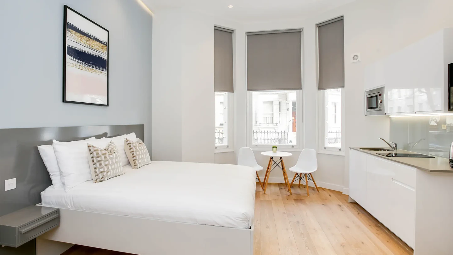 An elegant high-ceiling studio apartment with a comfortable double bed and practical kitchen area in the Kensington Serviced Apartments in Central London