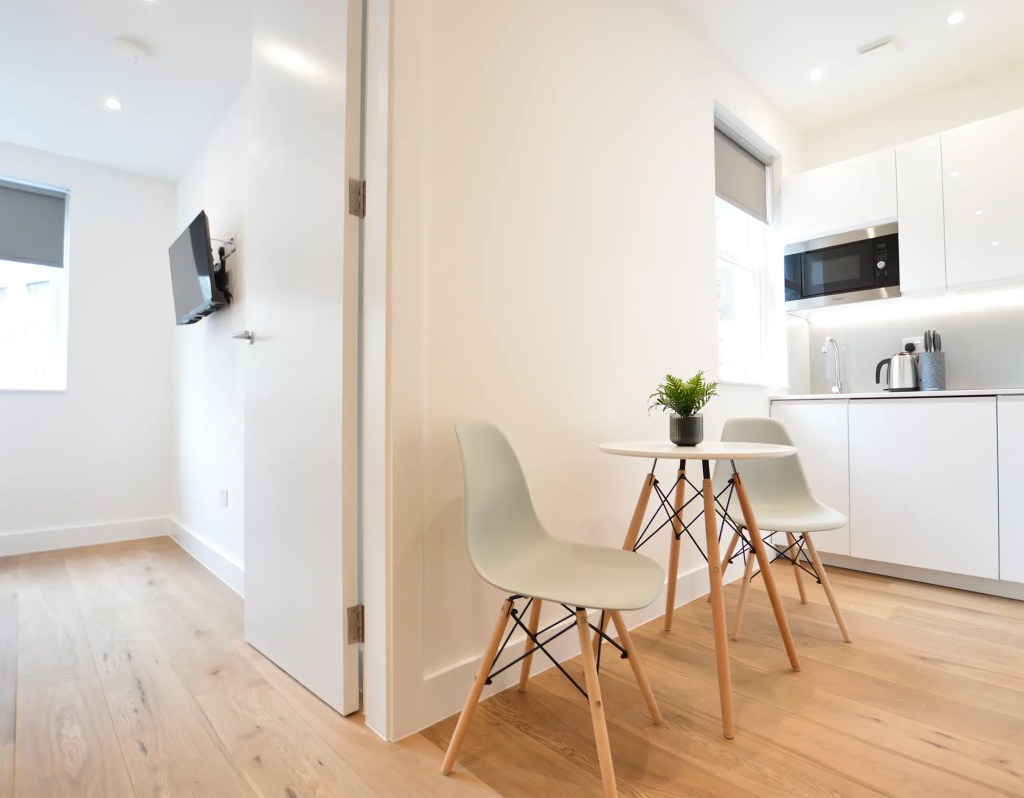 A comfortable living area with a dining table and a fully equipped kitchenette near a cozy bedroom with a double bed in a small one-bedroom apartment in Marylebone at 162 New Cavendish, London