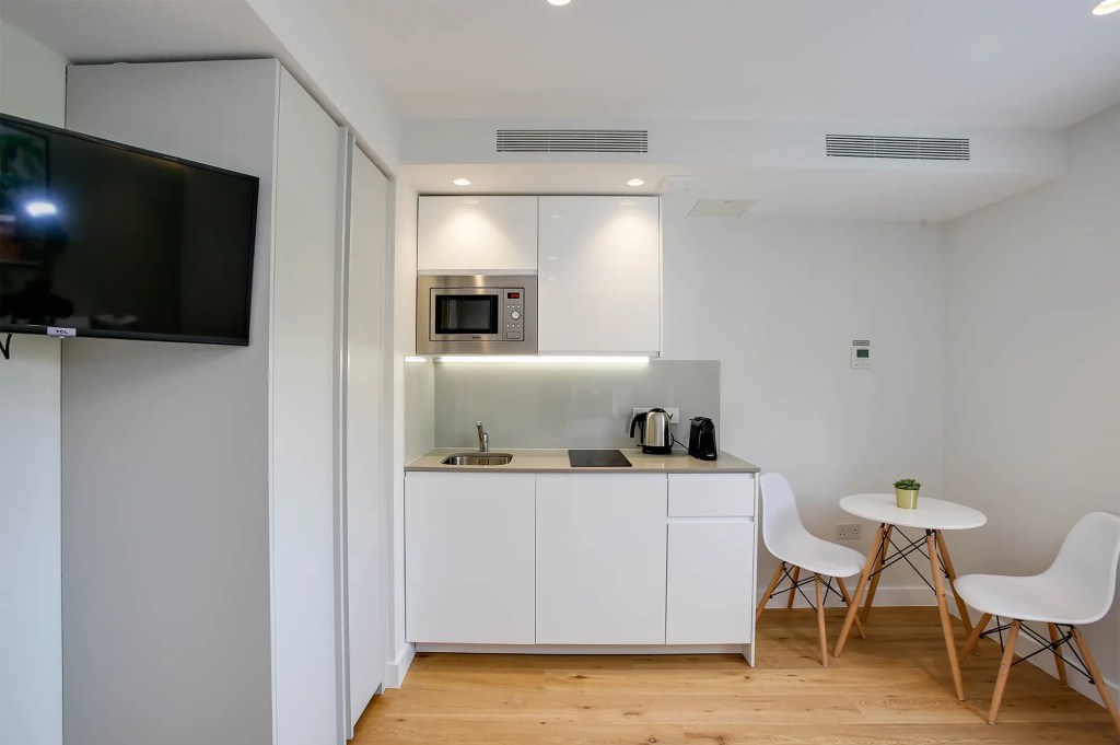 Elegant fully equipped kitchen, cozy dining area, and TV unit in a light-filled Cromwell studio apartment at 3 Knaresborough Place, Kensington, London