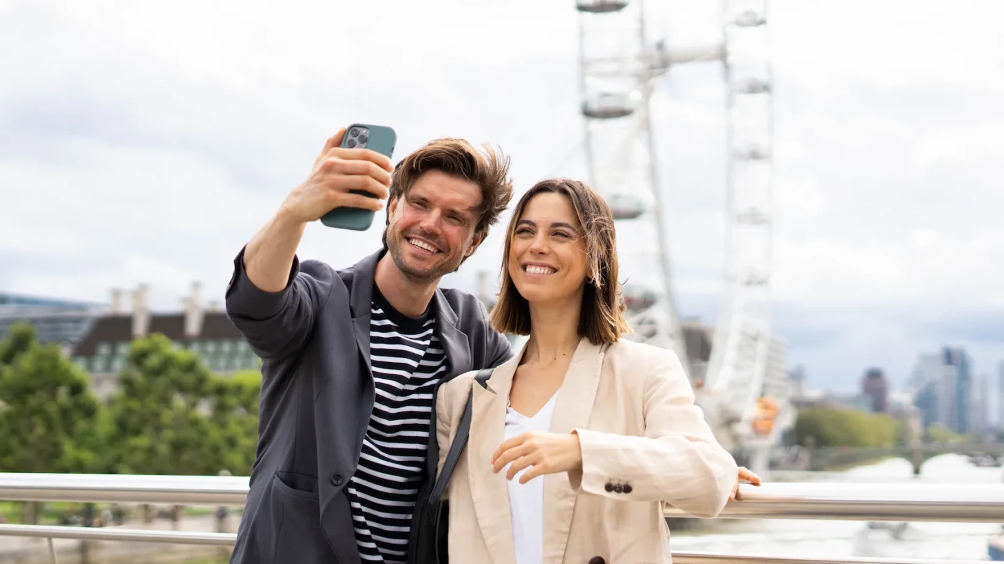 Young couple staying at StayPrime Serviced Apartments taking a picture of themselves in front of the London Eye in central London