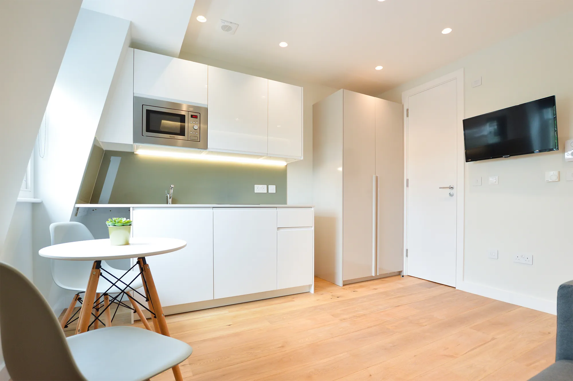 ully equipped kitchen adjacent to a dining area with a table and two chairs, complemented by a closet for ample storage space in a one-bedroom serviced apartment at Earl's Court.