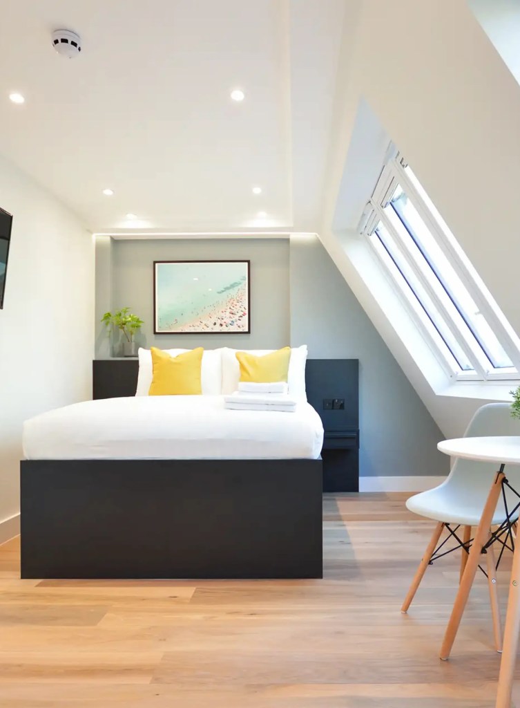 Light-filled studio with wooden floors, a double bed, cozy dining area, and roof windows at New Cavendish Serviced Apartments