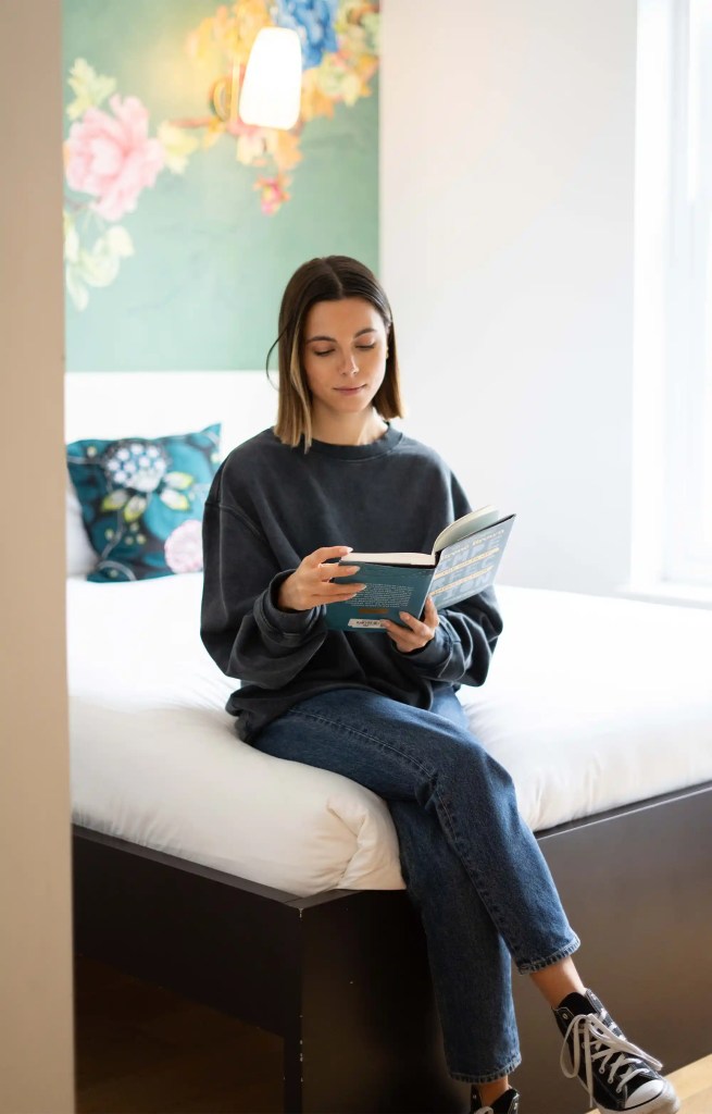 Young professional reading a book on a plush double bed in a Notting Hill serviced apartment near Portobello Road