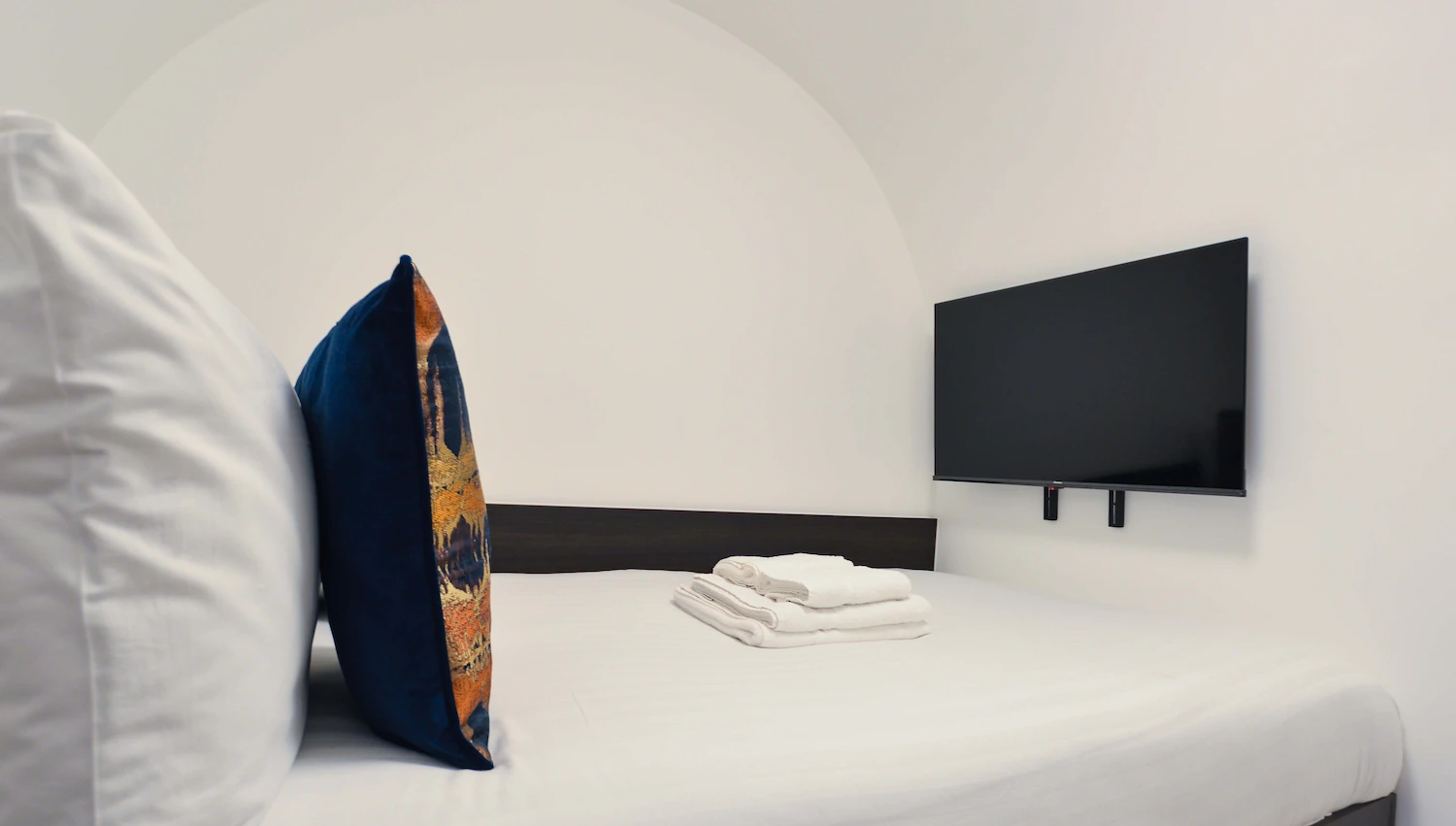 Single bed with modern linens, fresh towels, and a TV unit in a serviced single room in Fitzrovia, Central London