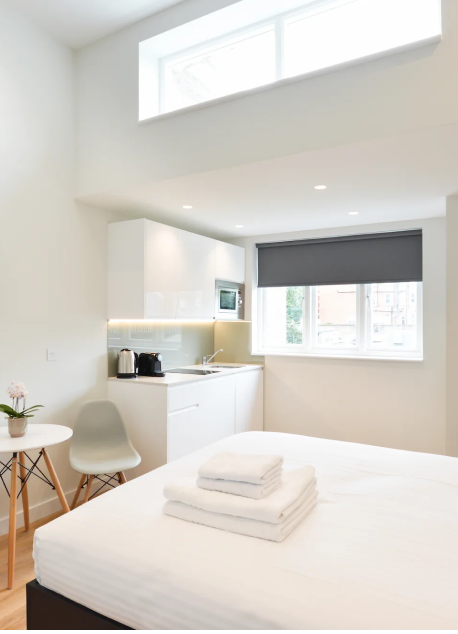 A bright long term let studio in central London, featuring wooden floors, a cozy double bed, and a dining area