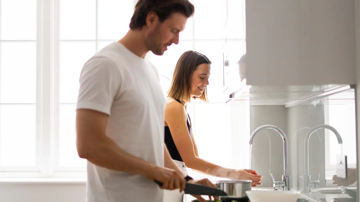 A young couple cooking together in a modern, fully equipped kitchen of a long term let at a Stayprime serviced apartment in London.