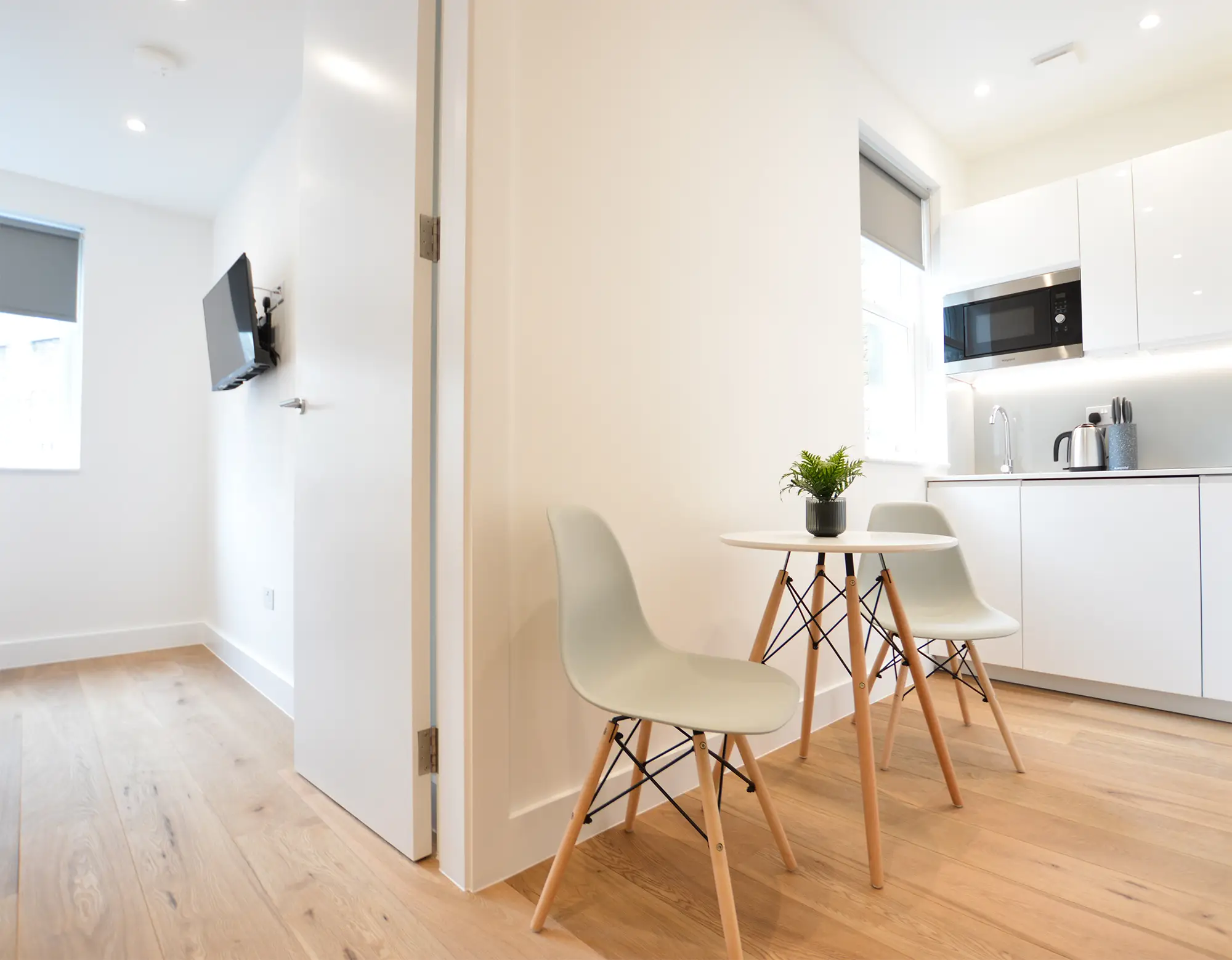 A bright one-bedroom apartment in London featuring a sleeping area, a desk, and a fully equipped modern kitchen.